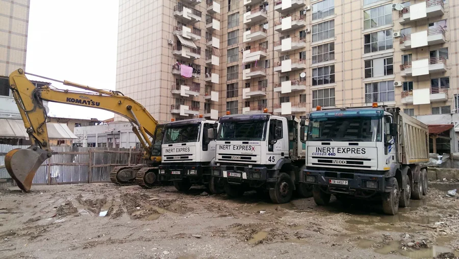Ekskavatorë dhe kamionë pranë ndërtesave në ndërtim