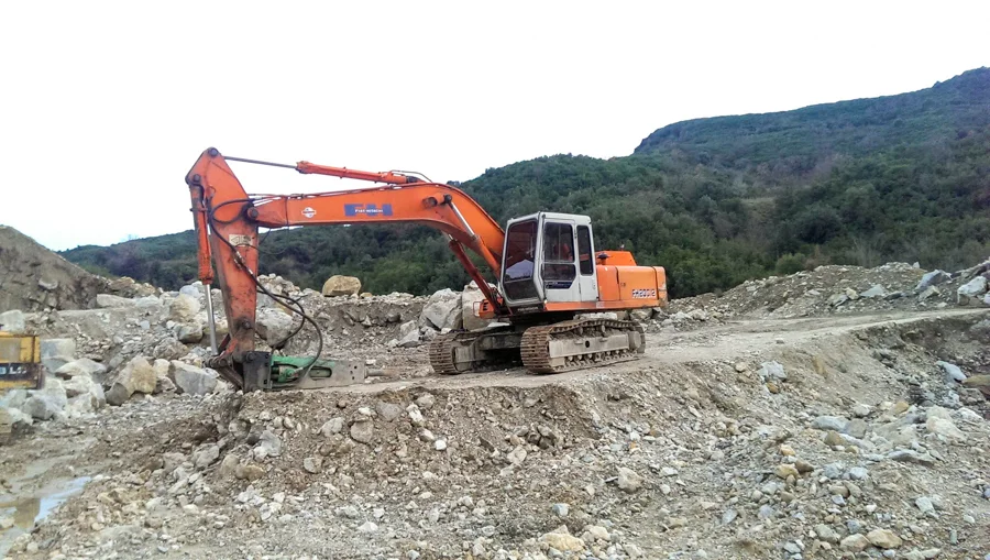 Ekskavator portokalli duke punuar në terren shkëmbor